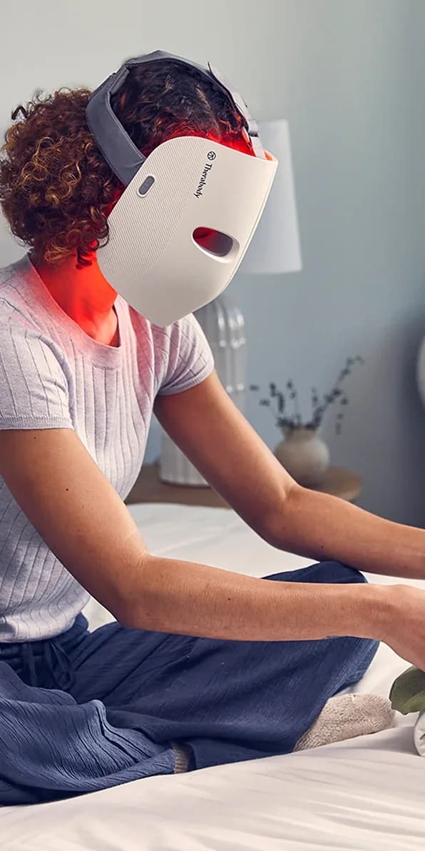 Une femme porte un masque de luminothérapie infrarouge allumé.